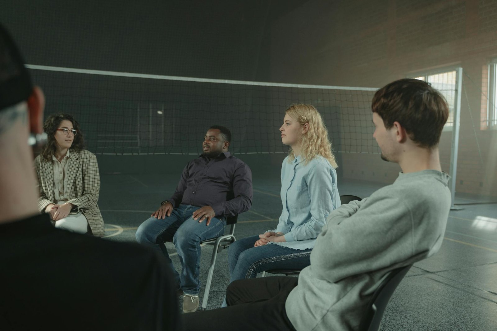 Diverse group of adults in a supportive indoor discussion setting. Sharing experiences.